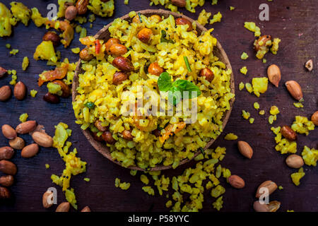 Close up indiano brunch popolare piatto in un vaso di argilla con secchi fritti sulla base di arachidi è Poha batata o Pava batata su una superficie in legno in dark Gothi Foto Stock