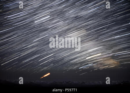 Un bellissimo panorama notturno del cielo stellato con tracce di meteore e stelle nella forma di piste circolari contro lo sfondo del Monte Nevoso Foto Stock