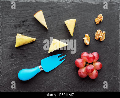 Vassoio di formaggi formaggi diversi con uve e mallo di noce nera sulla piastra di ardesia.vista superiore Foto Stock