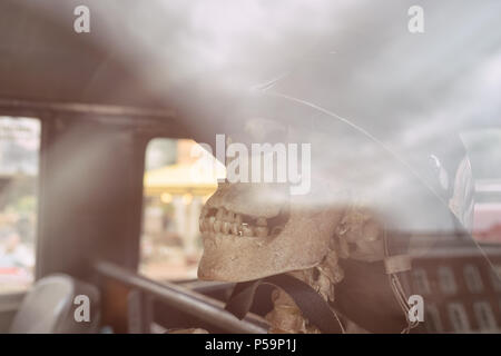 Un modello di un intonaco teschio umano con uno scheletro in un casco in auto salon con riflessi di luce e un riflesso delle case. Foto Stock