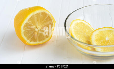 Un limone tagliato e due fette di limone nella lastra di vetro.bianco sullo sfondo di legno. Foto Stock