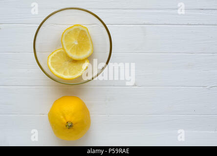 Un limone e due fette di limone nella lastra di vetro.Un limone è verso il basso e due fette di limone nella lastra di vetro sono sulla parte superiore.bianco sullo sfondo di legno.Copys Foto Stock