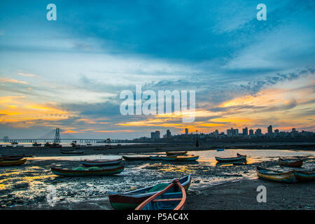 Silhouette di barche da pesca durante la bassa marea, tramonto vicino Mahim bay - Mumbai, Maharashtra, India. Worli Sea Link, Bandra Pali hill in background. Foto Stock