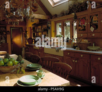 Piastre di verde e tazze sul tavolo di pino in cucina di paese di estensione con montati armadi di pino bianco e lavabo in ceramica Foto Stock