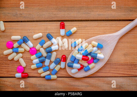 Pillole colorate e il farmaco in una cucina in legno cucchiaio, su tavole di legno sfondo, salute e concetto di medicazione Foto Stock