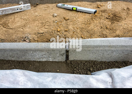 Impostazione di restrizioni di bordo acquistare mettendo cordolo di confine pietre in massa di calcestruzzo umido Foto Stock