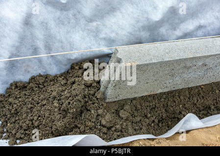 Impostazione di restrizioni di bordo acquistare mettendo cordolo di confine pietre in massa di calcestruzzo umido Foto Stock