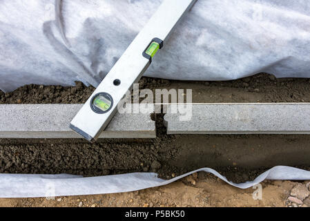 Impostazione di restrizioni di bordo acquistare mettendo cordolo di confine pietre in terra umida di calcestruzzo con bolla di livello Foto Stock