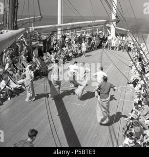 Degli anni Cinquanta, per passare il tempo, di divertirsi e di mantenere attivo durante un lungo viaggio, un'unione-castello steamship il viaggio a Cape in Sud Africa, maschio adulto passeggeri prendono parte a un gioco di coperta, il sacco tradizionale gara dove i concorrenti in sacchi o in sacchi postali salta da un punto di partenza per una linea finsh. Gli altri passeggeri seduti in sedie a sdraio allegria. Foto Stock