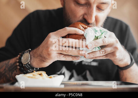 Giovane uomo barbuto mangiare hamburger. Foto Stock