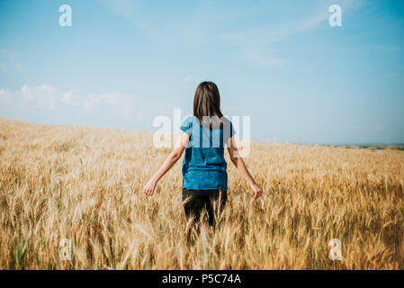 Donna che cammina attraverso il campo di grano, dolly shot. La mano della bambina toccando spighe di grano Foto Stock