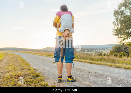 Padre portando la sua figlia sovrapponibile in estate Foto Stock