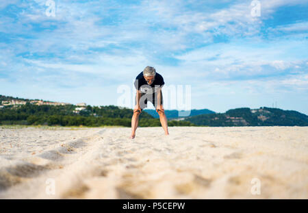 Stanco senior tenendo il resto durante l'esercizio sulla spiaggia, uno stile di vita attivo Foto Stock