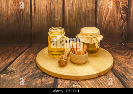 Golden miele in vasetti e bastoncini di cannella sul piatto di legno su sfondo di legno, close up Foto Stock