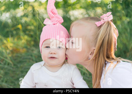 Due sorelle. La sorella di baci la sorella più giovane sulla guancia. Cappello rosa in un pisello e archi. Foto Stock