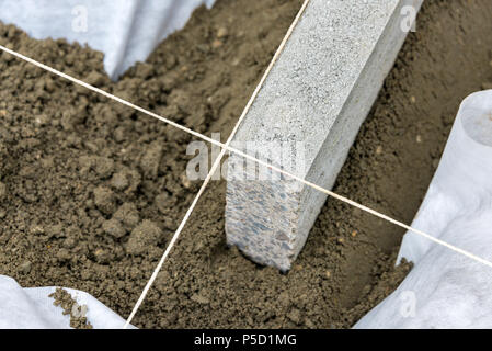Impostazione di restrizioni di bordo acquistare mettendo cordolo di confine pietre in massa di calcestruzzo umido Foto Stock