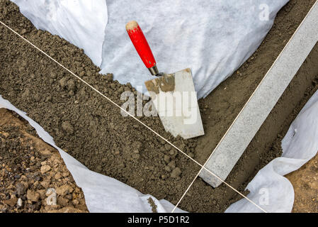 Impostazione di restrizioni di bordo acquistare mettendo cordolo di confine pietre in terra umida di calcestruzzo con cazzuola Foto Stock