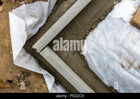 Impostazione di restrizioni di bordo acquistare mettendo cordolo di confine pietre in massa di calcestruzzo umido Foto Stock
