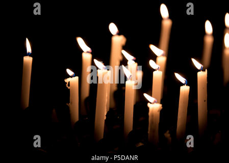 Molte candele accese - luce di candele nella chiesa su sfondo nero Foto Stock