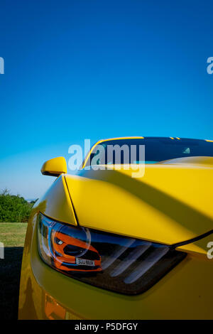 Un giallo Ford Mustang 5 litri V8 GT Fastback Auto con una seconda orange Ford Mustang riflessa nella lente del faro Foto Stock