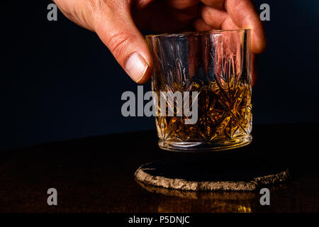 Una mano tenendo lontano un bicchiere di cristallo pieno di whiskey Foto Stock