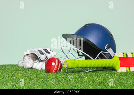 Cricket attrezzatura con bat, palla, casco e guanti in erba con sfondo verde. Foto Stock