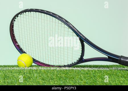 A tennis racket and ball on grass with plain green background. Foto Stock