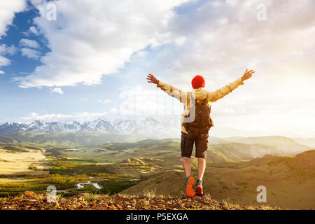 Felice turista sta con le braccia sollevate sulla collina contro montagne al tramonto Foto Stock