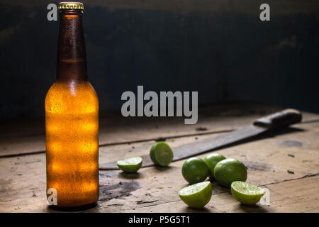 Vaso freddo di birra e limoni su una tavola in legno rustico, machete, Messico Foto Stock