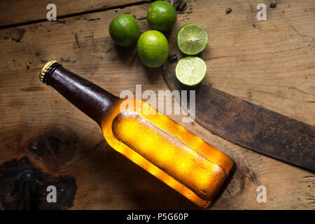 Vista dall'alto di un freddo bottiglia di birra e limoni su una tavola in legno rustico, machete, Messico Foto Stock