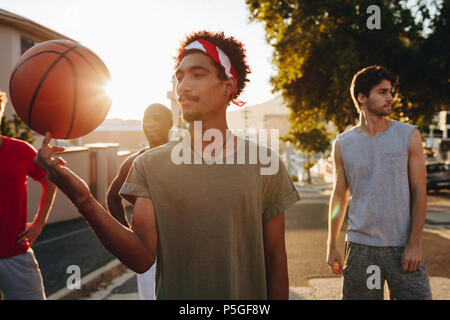 Quattro uomini di basket a piedi giù per la strada a suonare con la palla. Uomo di pallacanestro di filatura sul suo dito. Foto Stock