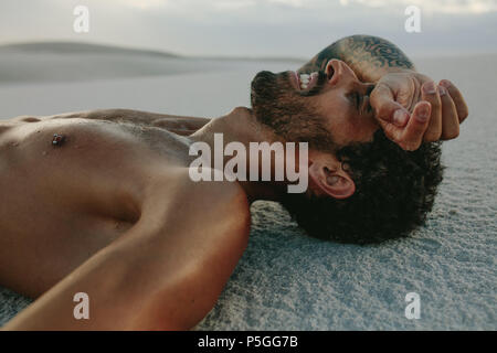 Stanco uomo relax dopo un intenso allenamento. Atleta prendendo appoggio sulla sabbia dopo un allenamento. Foto Stock