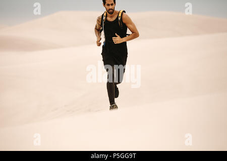 Montare il giovane uomo che corre sulle dune di sabbia. Runner che esercitano nel deserto. Foto Stock