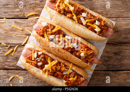 Autentico chili di hot dog con il formaggio cheddar e cipolla e salsa piccante di close-up su carta sul tavolo. parte superiore orizzontale vista da sopra Foto Stock