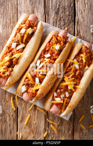 Autentico chili di hot dog con il formaggio cheddar e cipolla e salsa piccante di close-up su carta sul tavolo. verticale in alto vista da sopra Foto Stock