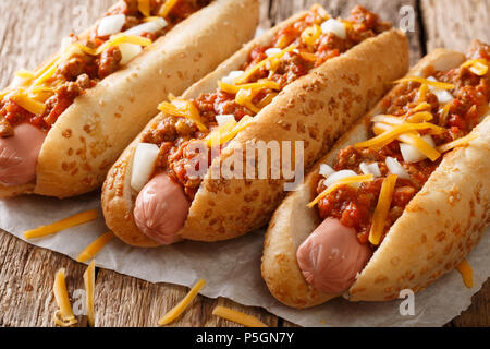 Autentico chili di hot dog con il formaggio cheddar e cipolla e salsa piccante di close-up su carta sul tavolo orizzontale. Foto Stock