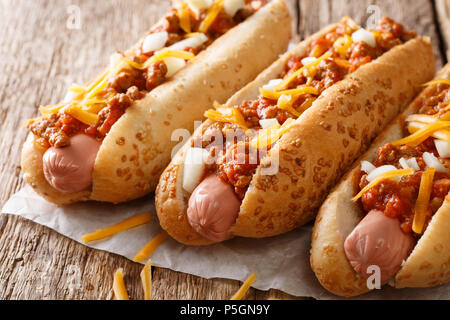 American fast food: chili hot dogs con il formaggio cheddar, manzo piccante tritare la cipolla e salsa di close-up sul tavolo. orizzontale, stile rustico Foto Stock