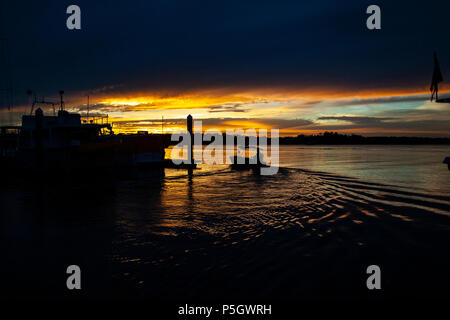 Un impressionante e ispiratore di color rosso NUVOLOSO TRAMONTO marina seascape oltre l'acqua di mare con acqua riflessioni. Catturate in barattolo di latta Bay, Queensland, Austra Foto Stock