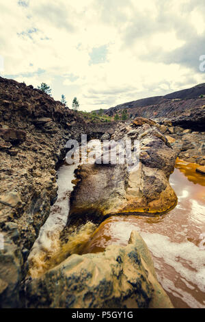 Una piccola cascata di acqua rossa tra rocce colorate da minerali in miniera Zaranda, Spagna Foto Stock