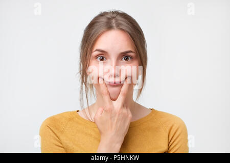 Colpo di caucasici bella ragazza adolescente forzando un sorriso, tenendo le dita in corrispondenza dei bordi delle labbra Foto Stock