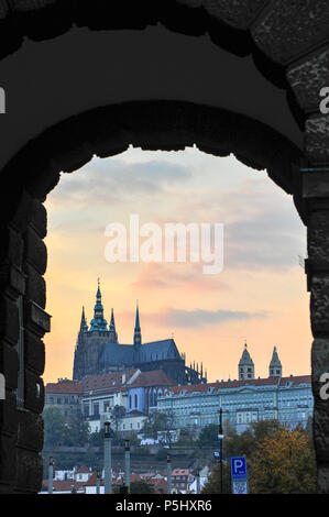 Il Castello di Praga e la Cattedrale di San Vito come tramonto. Vista pittoresca attraverso un arco di pietra nella città vecchia Foto Stock