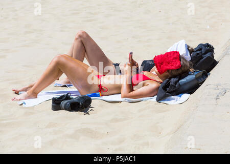 Bournemouth Dorset, Regno Unito. Il 27 giugno 2018. Regno Unito: meteo sunseekers testa per le spiagge a Bournemouth su un altro bel giorno caldo e soleggiato con ininterrotta in un cielo azzurro e sole. Una piacevole brezza oggi rende il calore più sopportabile. Due giovani donne a prendere il sole in bikini con il volto coperto. Credito: Carolyn Jenkins/Alamy Live News Foto Stock