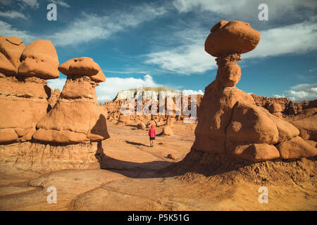 Vista panoramica di un escursionista in giacca rossa a piedi in Goblin Valley State Park in mezzo a bellissimi hoodoos formazioni arenarie, Utah, Stati Uniti d'America Foto Stock