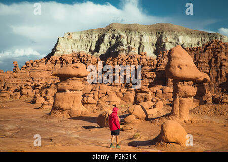 Vista panoramica di un escursionista in giacca rossa a piedi in Goblin Valley State Park in mezzo a bellissimi hoodoos formazioni arenarie, Utah, Stati Uniti d'America Foto Stock