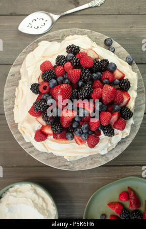 Pavlova meringa dessert torta fatta con fragole, more, lamponi e mirtilli, piantati su una piattaforma di granito Foto Stock