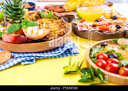 Diversi tipi di frutta e verdura in grigliate e gamberetti. Sfondo giallo. In estate la cena. Spazio di copia Foto Stock
