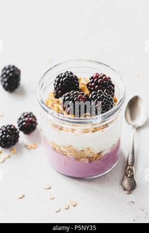 Colazione sana parfait con blackberry, yogurt e granola in un recipiente su cemento bianco sullo sfondo. Uno stile di vita sano, mangiare sano concetto Foto Stock