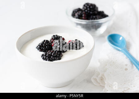 Lo yogurt greco con more nella ciotola bianco su sfondo bianco, primo piano Foto Stock