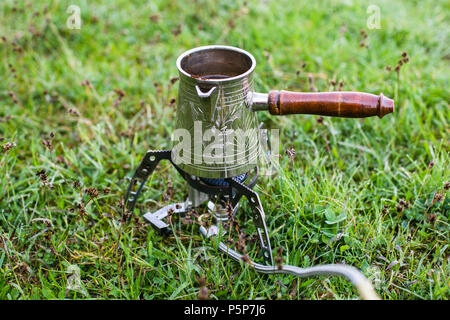 Piccolo campeggio fornello a gas e piccole cezve caffè la mattina sull'erba Foto Stock