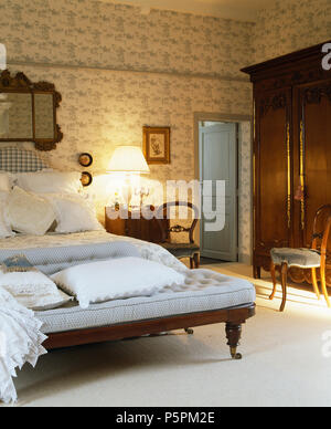 Blu pallido divano ai piedi del letto con lenzuola bianche nel paese francese camera con Toile de Jouy wallpaper Foto Stock